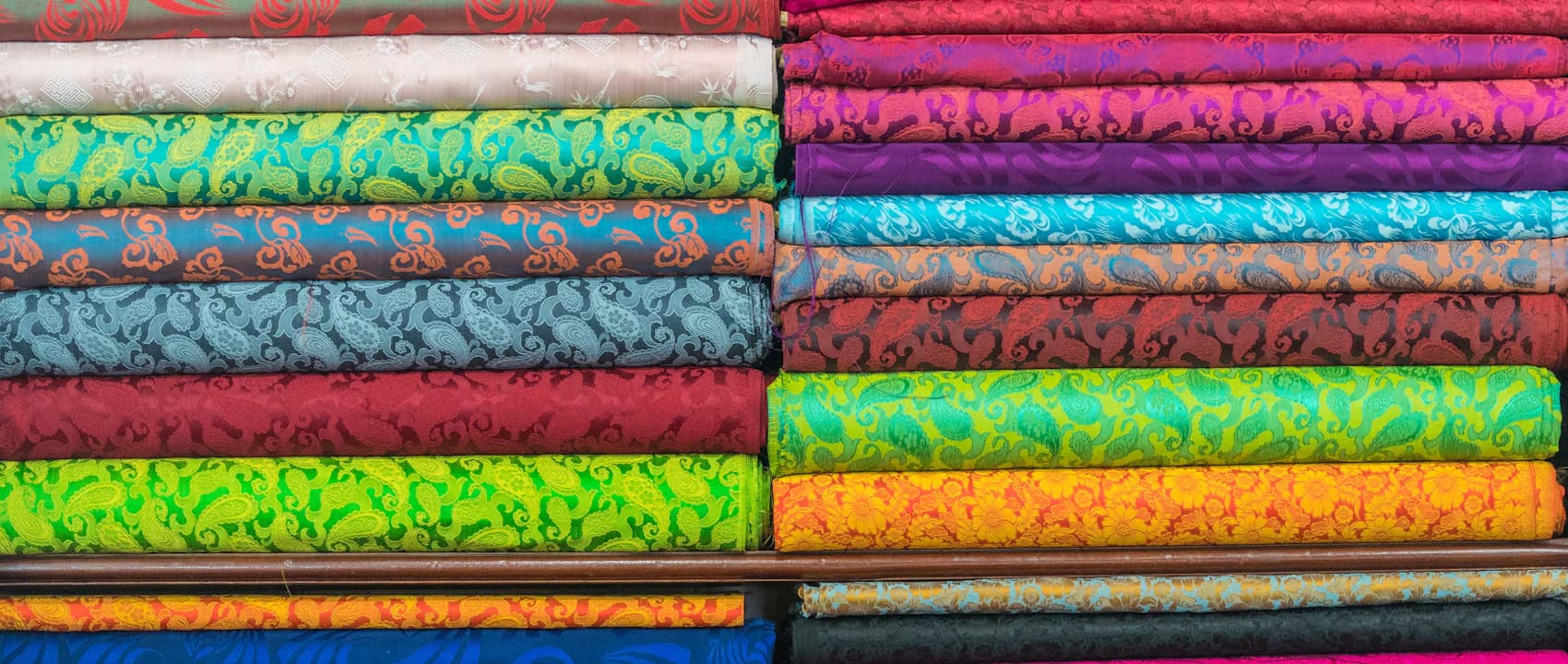 Stacks of brightly coloured patterned fabric bolts on a showroom shelf